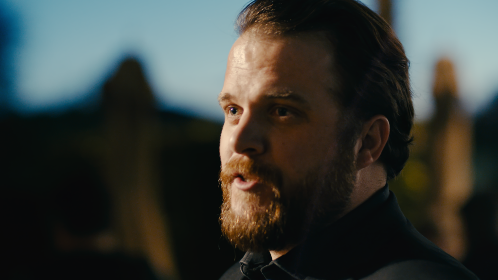 Bearded man in period dress, lit by low golden light